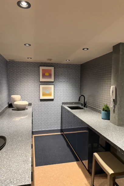 Cambridge Lounge kitchenette with patterned walls, stone countertops, a sink, and framed artwork.